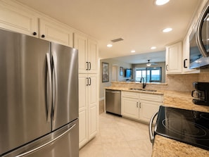 A modern kitchen with stainless steel appliances, white cabinetry, and a large island with a sink.