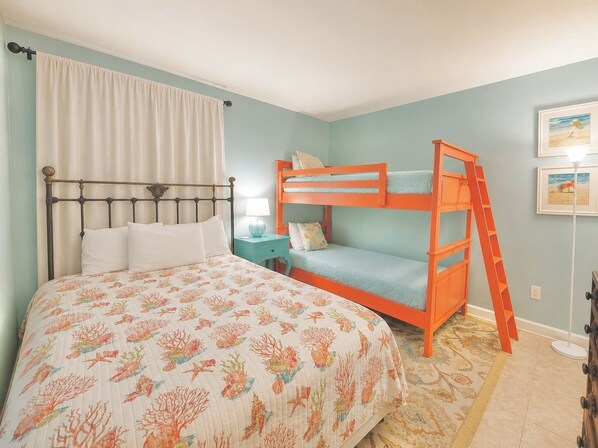 A bedroom with a bunk bed, a bed with a floral bedspread, a nightstand, a lamp, and a framed picture on the wall.