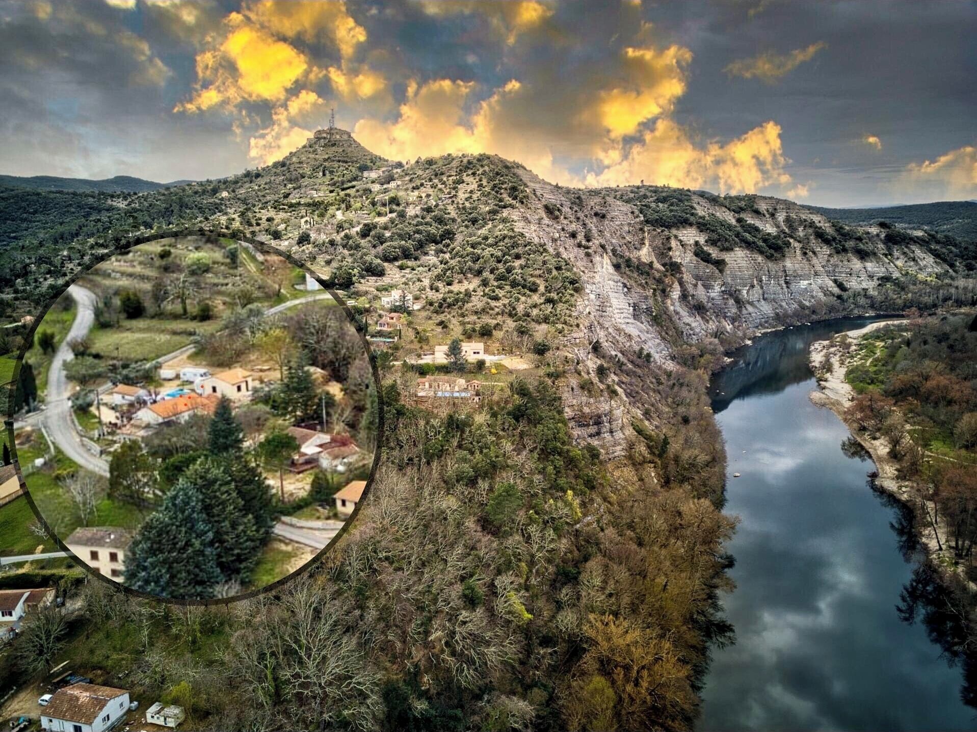 Un paysage montagneux avec une rivière, un petit village et une colline imposante surmontée d’une tour.