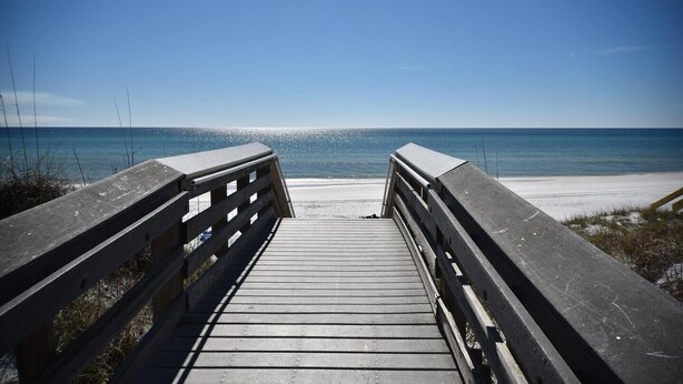 Ein Holzsteg führt zu einem Strand bei blauem Himmel.