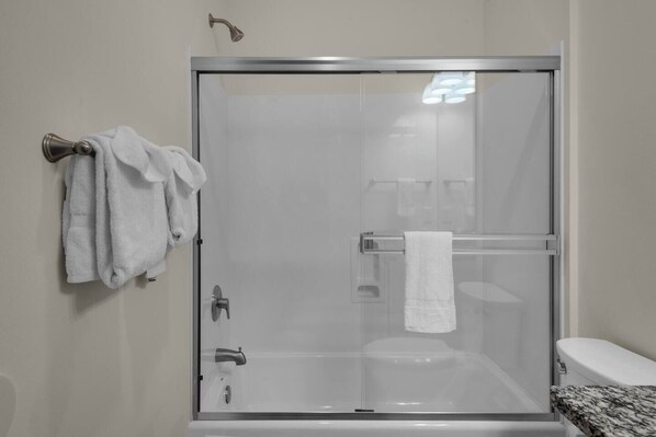 A glass-enclosed shower with a towel rack, a toilet, and a marble countertop.