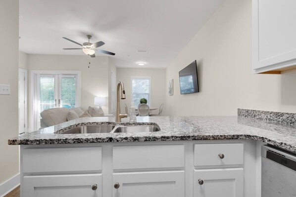 A kitchen with a granite countertop, white cabinetry, a ceiling fan, and a dining area in the background.
