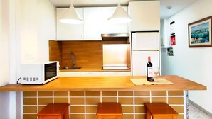 Una cucina moderna con pensili bianchi, un piano di lavoro in legno e due lampade a sospensione. Si vedono un forno a microonde, una bottiglia di vino e un bicchiere sul bancone.