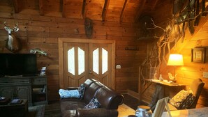Ein gemütliches Blockhaus-Interieur mit einem Ledersofa, einem Holzesstisch und einem Fernseher auf einem Schrank.