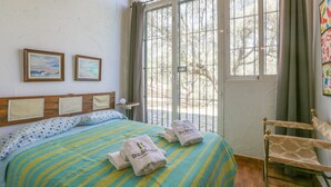 A bedroom with a bed, two framed pictures, a window, and a chair. - Casa rural Navalonguilla Santa Olalla del Cala by Ruralidays (Huelva)