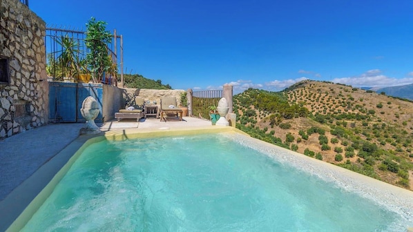 Una piscina con muro de piedra y mobiliario exterior, rodeada por un paisaje montañoso.