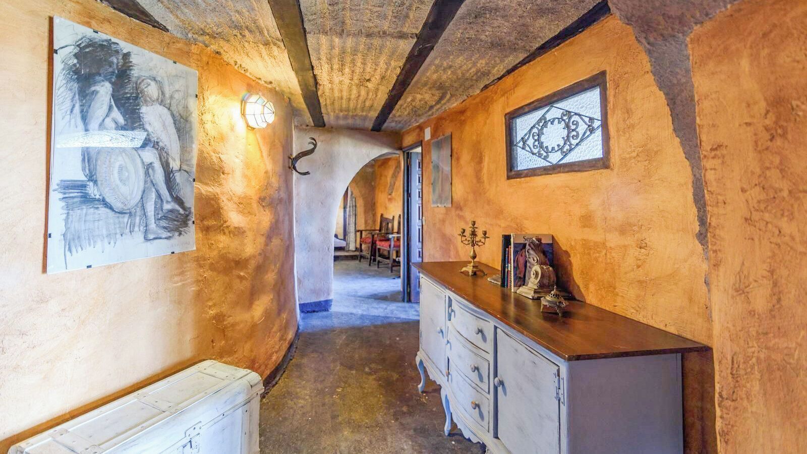 Un couloir étroit aux murs rustiques, un meuble en bois et un chandelier.
