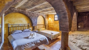 Una habitación rústica con una cama grande, una cama más pequeña y un arco de piedra.