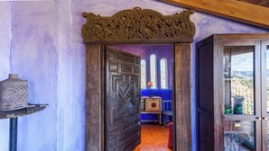 Ein Zimmer mit Holztür, einem kleinen Tisch mit Lampe und Blick durch ein Fenster.