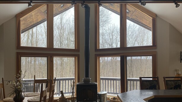 A spacious living room with a large fireplace, wooden flooring, and large windows offering a view of the outdoors. - Irish Hill Chalet (West Valley)