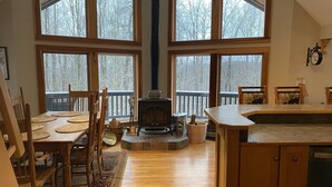 A spacious kitchen with large windows, a wood-burning stove, and a dining area with chairs and a rug. - Irish Hill Chalet (West Valley)