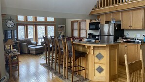 A spacious kitchen with wooden cabinets, a central island with bar stools, a microwave, and a refrigerator. - Irish Hill Chalet (West Valley)