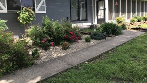 Una casa moderna con fachada gris, un porche cubierto y un jardín cuidado con diversas plantas y flores.