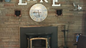 Una chimenea con un reloj encima, techo de madera y pared de piedra.