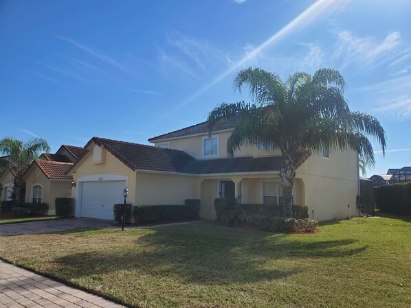 A two-story house with a tiled roof, a garage, and a well-maintained lawn. - Beautiful Vacation Home, Quiet Neighborhood, Sunny South Facing Pool (Davenport)