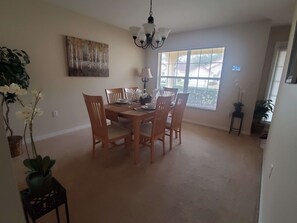 A dining area with a wooden table and chairs, a chandelier, and a large window with blinds. - Beautiful Vacation Home, Quiet Neighborhood, Sunny South Facing Pool (Davenport)
