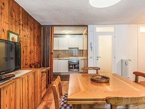 Un intérieur en bois comprenant une table à manger, des chaises, un téléviseur et un coin cuisine avec des placards et une cuisinière.