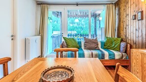 Een houten eettafel met een decoratief bord, een houten bank met kussens, en uitzicht op een balkon met een hekwerk en beplanting.