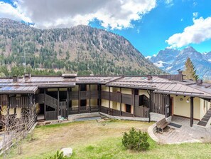 Un bâtiment de style chalet, avec une façade en bois, un espace extérieur aménagé et couvert, et une vue sur une chaîne de montagnes boisées.