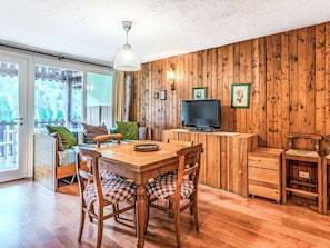 Interior de madera con una mesa de comedor, sillas, un televisor y un ventanal corredero que da a un área exterior.