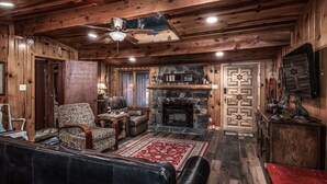 A cozy log cabin interior with a fireplace, leather furniture, and a stone wall. - Cabin on Bear Creek (Ruidoso)