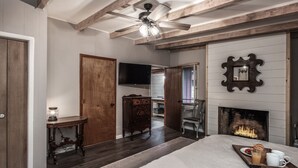 A bedroom with a bed, a wooden dresser, a television, a fireplace, and a ceiling fan. - Cabin on Bear Creek (Ruidoso)