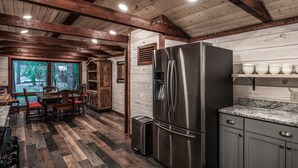 A modern kitchen with a stainless steel refrigerator, wooden flooring, and a view of the outdoors. - Cabin on Bear Creek (Ruidoso)