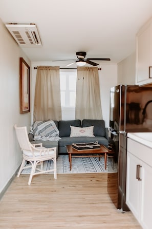 A compact living space with a sofa, a chair, a coffee table, a ceiling fan, and a refrigerator.