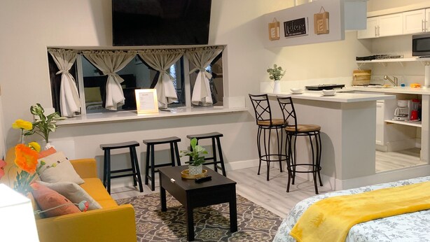 A modern living room with a sofa, coffee table, and a TV. There is a small kitchen area with a microwave and a dining table. - Private Studio, own entry, kitchenette,  full bath. (North Las Vegas)