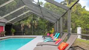 A covered pool area with lounge chairs and a glass enclosure. - Palm Palace - 2 House Compound Sleeps Up to 22!  Huge Pool and near the beaches (Fort Myers)