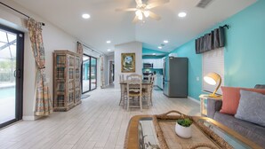 A spacious living area with a dining table, sofa, and a ceiling fan. - Palm Palace - 2 House Compound Sleeps Up to 22!  Huge Pool and near the beaches (Fort Myers)