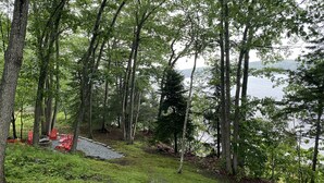 Ein bewaldetes Gebiet mit einem See im Hintergrund, roten Adirondack-Stühlen und einem Kiesweg.