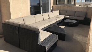 An outdoor seating area with a long sofa and two side tables, a sliding glass door, and a window. - ON THE SAND! (Oxnard)