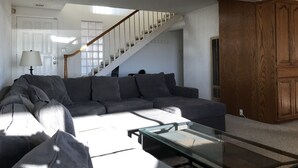 A living room with a gray sectional sofa, a glass coffee table, a wooden cabinet, and a staircase leading to another level. - ON THE SAND! (Oxnard)