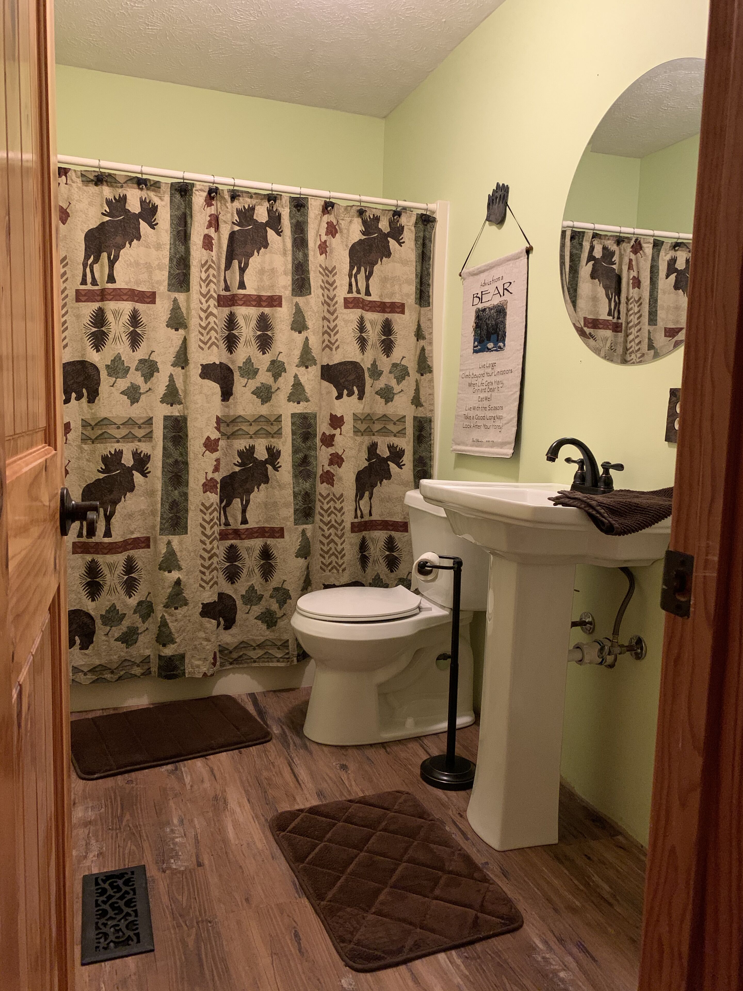 Un baño con inodoro, lavabo y cortina de ducha con estampado de alce y bosque.