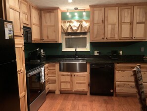 Kitchen features a stainless steel sink, dishwasher, and stove, with a window and overhead lighting.
