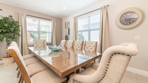 Une salle à manger avec une table en verre, six chaises rembourrées, un vase décoratif et une horloge murale.