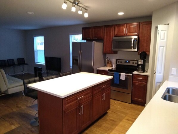 A modern kitchen with wooden cabinets, stainless steel appliances, and a central island. - ⁂ Memory Foam Bed, Blackout Curtains & Smart TV (Renton)