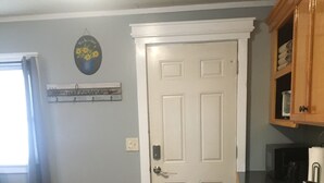 A kitchen with a white door, a black mat, a tiled floor, and wooden cabinets. - Home Away From Home, Newly Renovated Apartment (North Troy)