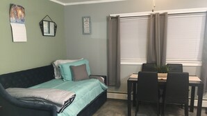 A cozy room with a bed, a dining table with chairs, and a window with curtains. - Home Away From Home, Newly Renovated Apartment (North Troy)