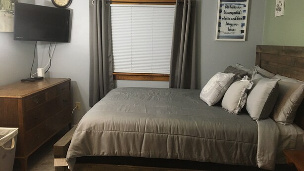 A bedroom with a bed, a wooden dresser, a television, and a window with curtains. - Home Away From Home, Newly Renovated Apartment (North Troy)