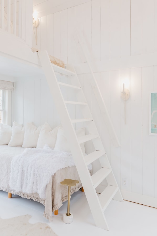 Quarto branco com cama, escada branca e parede branca.