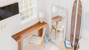 Ein Zimmer mit einer hölzernen Bank, einem runden Korbstuhl, einem großen Spiegel und einem Surfbrett, das an der Wand lehnt.