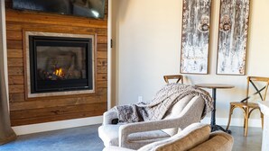 Una sala de estar acogedora con chimenea, un sillón cómodo, una mesita redonda y dos sillas de madera.