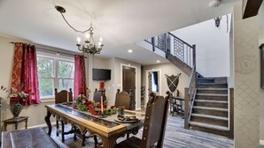 Comedor con mesa de madera, sillas y una araña. Una escalera conduce a un nivel superior.