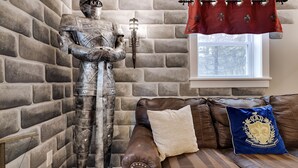 Una estatua de un caballero medieval junto a un sofá de cuero marrón con cojines decorativos, sobre un fondo de pared de ladrillo.