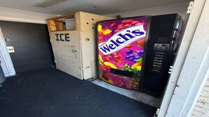 Màquina expenedora amb begudes de fruita Welch's, una porta amb la inscripció 'ICE' i un marc de porta obert parcialment.