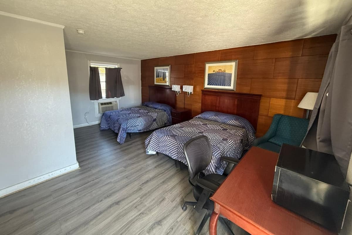 A room with two beds, a desk, a chair, a lamp, and a window with curtains.