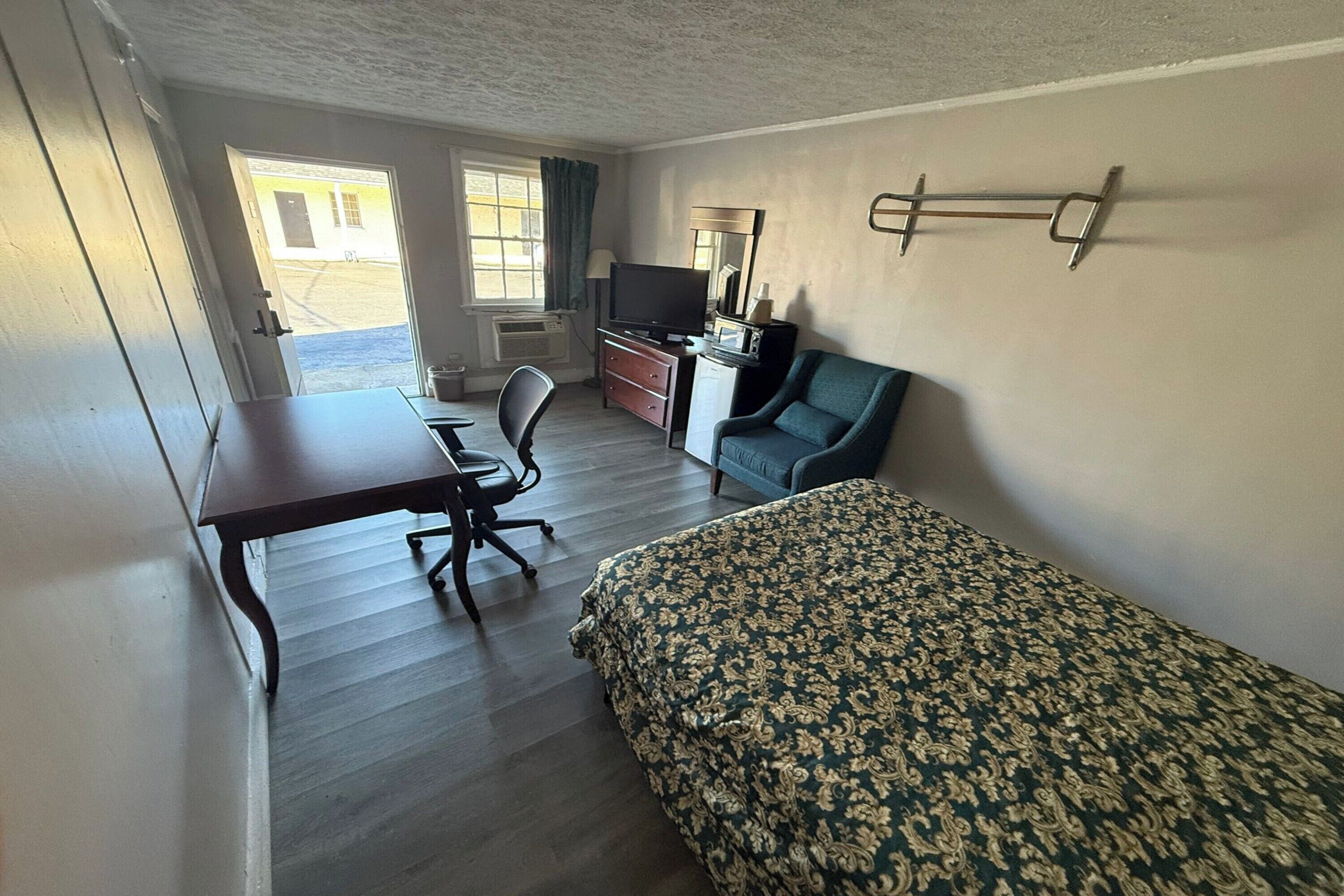 A room with a bed, a desk, a chair, a television, and a window.