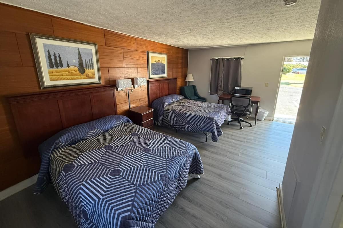 A hotel room with two beds, a desk, a chair, and a window with curtains.